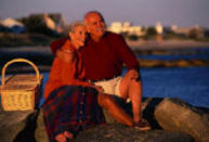 older couple at the seashore snuggling with picnic basket